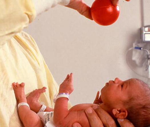 医生在一个新生婴儿上握着一个小红球。