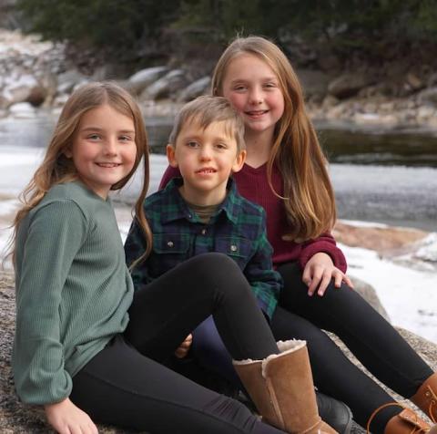 两个女孩和一个男孩兄弟姐妹坐在河边的岩石上